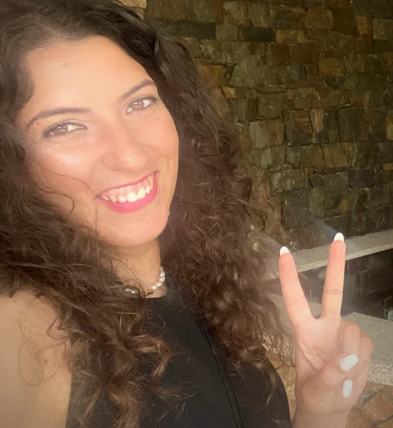 A Angie a sorrir para a câmara, de caracóis castanhos soltos, a fazer o sinal de paz com a mão