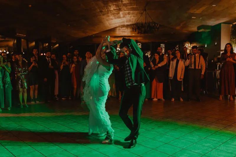 Noivos a dançar a primeira dança numa pista iluminada, rodeados pelos convidados